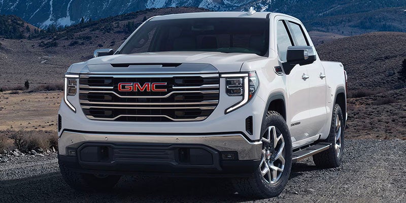 White 2025 GMC Sierra truck parked on gravel in front of snowcapped mountains